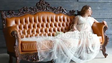 穿着豪华礼服的怀孕新娘正坐在皮沙发上
